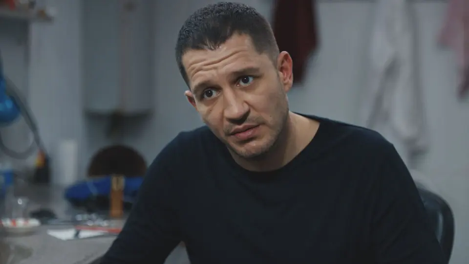Yeraltı 20. bölümden sahne: siyah tişörtlü bir erkek karakter iç mekânda karşısındakiyle konuşuyor.